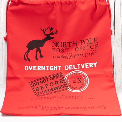 Christmas Gift Bags | Reusable Oversized Fabric with Drawstring Cord - North Pole Post Office Overnight Delivery Logo - Alicia GonzalezGift Bags